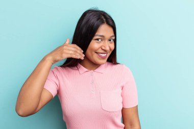 Genç Venezuelalı bir kadın mavi arka planda izole edilmiş bir şekilde bir şeylere gülüyor, elleriyle ağzını kapatıyor..