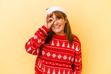 Middle age caucasian woman celebrating Christmas isolated on yellow background excited keeping ok gesture on eye.