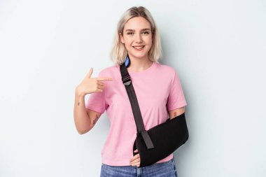 Kırık elli beyaz bir kadın mavi arka planda izole edilmiş. Gömlek fotokopi alanını işaret ediyor. Gururlu ve kendinden emin.