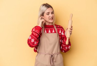 Beyaz tenli fırıncı kadın Noel için kurabiye yapıyor sarı arka planda izole edilmiş kulakları elleriyle kapatıyor..