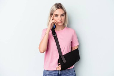 Kırık elli beyaz bir kadın mavi arka planda izole edilmiş. Şakağı işaret ediyor, düşünüyor, bir göreve odaklanıyor..