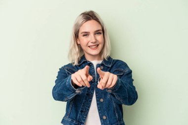 Yeşil arka planda izole edilmiş genç beyaz kadın parmaklarıyla ön tarafı işaret ediyor..