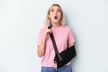 Kırık elli beyaz bir kadın mavi arka planda izole edilmiş, ağzı açık, üst tarafı işaret ediyor..