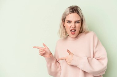 Yeşil arka planda izole edilmiş genç beyaz kadın işaret parmaklarıyla fotokopi alanını işaret ederek heyecan ve arzusunu ifade ediyor..