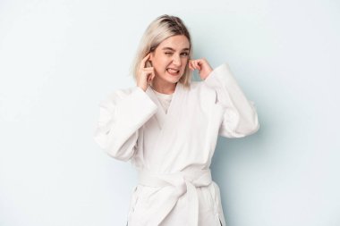 Mavi arka planda karate yapan beyaz bir kadın. Kulaklarını elleriyle kapatıyor..