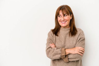 Beyaz arka planda soyutlanmış orta yaşlı beyaz kadın kollarını kavuşturarak gülümsüyor..