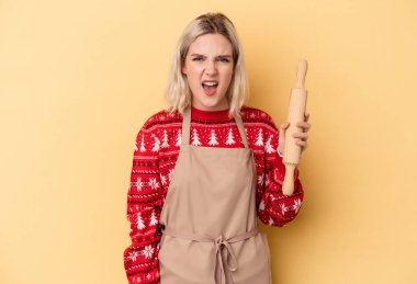 Kafkasyalı genç fırıncı kadın Noel için kurabiye yapıyor sarı arka planda izole edilmiş çok kızgın ve agresif çığlıklar atıyor..