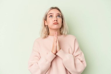 Yeşil arka planda izole edilmiş genç beyaz kadın el ele tutuşup dua ediyor, kendine güveniyor..