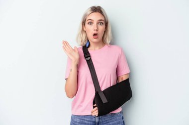 Kırık elli beyaz bir kadın mavi arka planda izole edilmiş, şaşırmış ve şok olmuş..