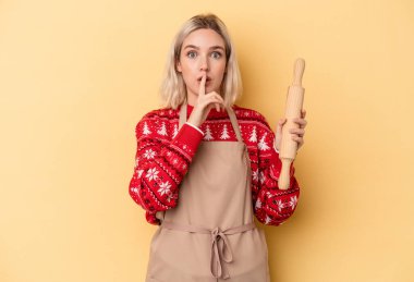 Beyaz tenli genç fırıncı kadın Noel için kurabiye yapıyor sarı arka planda izole edilmiş ya sır saklıyor ya da sessizlik istiyor..