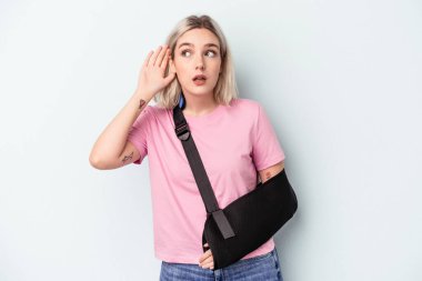 Kırık elli beyaz bir kadın mavi arka planda izole edilmiş bir şekilde bir dedikoduyu dinlemeye çalışıyor..