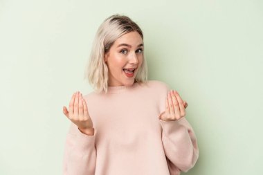 Yeşil arka planda izole edilmiş genç beyaz kadın sanki seni davet ediyormuş gibi seni işaret ediyor..