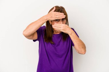 Beyaz arka planda izole edilmiş orta yaşlı beyaz kadın kameraya parmaklarıyla göz kırpıyor, yüzünü kapatmaktan utanıyor..