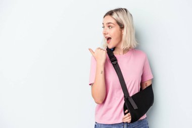 Kırık elli beyaz bir kadın mavi arka planda izole edilmiş, başparmak uzakta, gülen ve kaygısız..