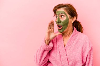 Middle age caucasian woman wearing a facial mask isolated on pink background is saying a secret hot braking news and looking aside