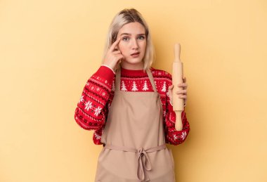 Beyaz tenli fırıncı kadın Noel için kurabiye yapıyor sarı arka planda izole edilmiş işaret parmağıyla hayal kırıklığı jesti gösteriyor..