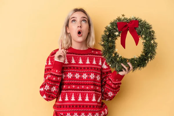 Mladá Běloška Drží Vánoční Věnec Izolované Žlutém Pozadí Ukazuje Vzhůru — Stock fotografie