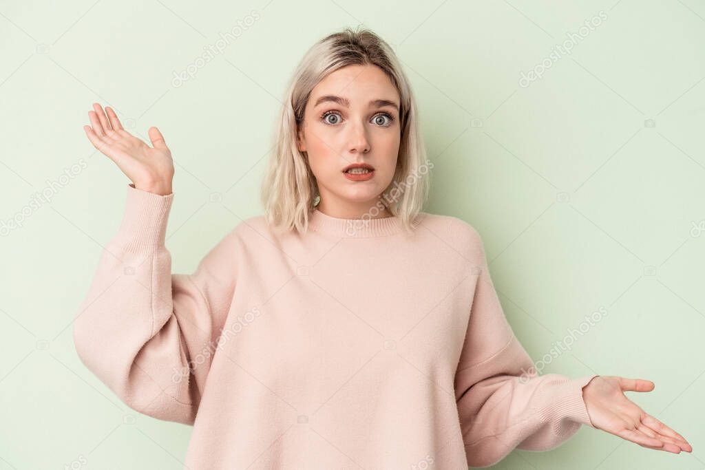 Young caucasian woman isolated on green background confused and doubtful shrugging shoulders to hold a copy space.