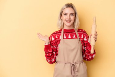 Beyaz tenli genç fırıncı kadın, sarı arka planda izole edilmiş kurabiyeler yapıyor. Bir avuç içinde fotokopi alanı var ve başka bir eli belinde tutuyor..