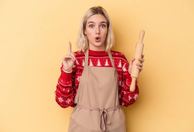 Kafkasyalı genç fırıncı kadın Noel için kurabiye yapıyor sarı arka planda izole edilmiş harika bir fikri var, yaratıcılık kavramı..