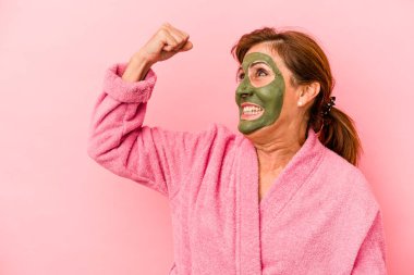 Middle age caucasian woman wearing a facial mask isolated on pink background raising fist after a victory, winner concept.