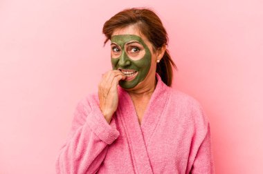 Middle age caucasian woman wearing a facial mask isolated on pink background biting fingernails, nervous and very anxious.