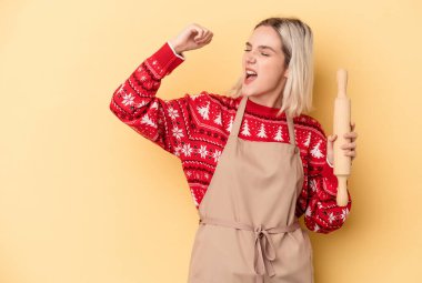 Genç Kafkas fırıncı kadın Noel için kurabiye yapıyor sarı arka planda izole edilmiş zafer kazandıktan sonra yumruğunu kaldırıyor, kazanan konsept..