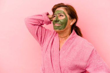 Middle age caucasian woman wearing a facial mask isolated on pink background touching back of head, thinking and making a choice.