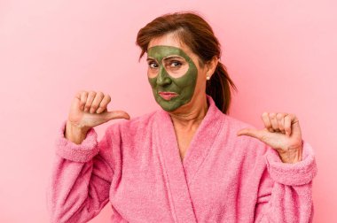 Middle age caucasian woman wearing a facial mask isolated on pink background feels proud and self confident, example to follow.