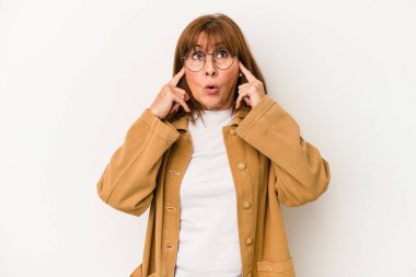 Beyaz arka planda izole edilmiş orta yaşlı beyaz bir kadın parmaklarıyla kulaklarını kapatıyor, gürültülü bir ortam yüzünden stresli ve çaresiz..