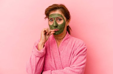 Middle age caucasian woman wearing a facial mask isolated on pink background with fingers on lips keeping a secret.