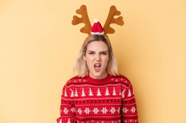 Sarı arka planda izole edilmiş, yılbaşı geyiği şapkası takan Kafkasyalı genç bir kadın çok sinirli ve agresif bir şekilde bağırıyor..