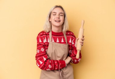 Beyaz tenli fırıncı kadın Noel için kurabiye yapıyor. Sarı arka planda izole edilmiş gülüyor ve eğleniyor..