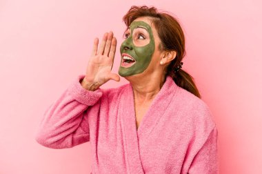 Middle age caucasian woman wearing a facial mask isolated on pink background shouting and holding palm near opened mouth.