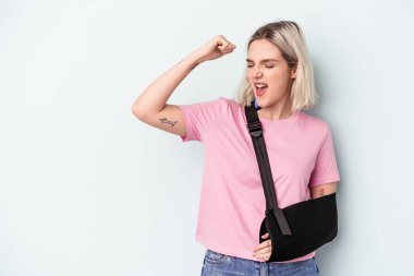 Kırık elli beyaz bir kadın mavi arka planda izole edilmiş zafer sonrası yumruğunu kaldırıyor, kazanan konsept..