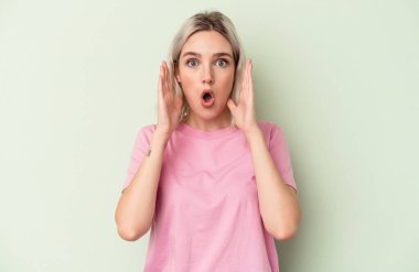 Yeşil arka planda izole edilmiş genç beyaz kadın şaşırdı ve şok oldu..