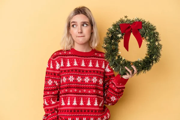 Jonge Blanke Vrouw Met Een Kerstkrans Geïsoleerd Gele Achtergrond Verward — Stockfoto