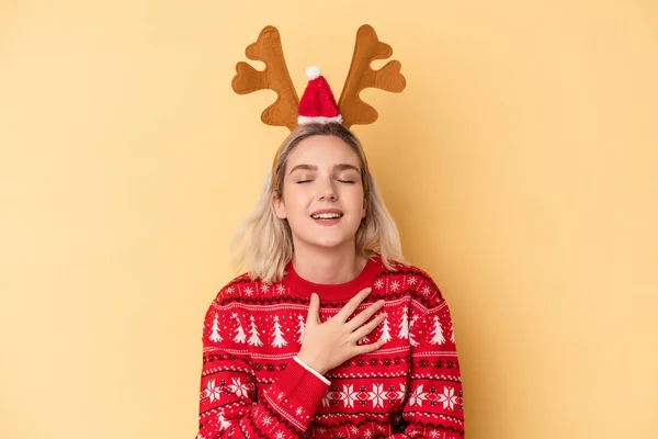 若いですCaucasian女性身に着けていますクリスマストナカイ帽子孤立した上に黄色の背景笑アウト大声で手に胸 — ストック写真