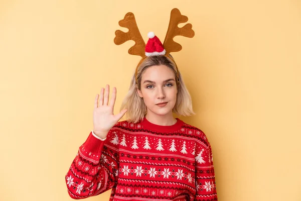 年轻的高加索女人戴着一顶黄色背景的圣诞驯鹿帽 高兴地微笑着 带着五号手指 — 图库照片