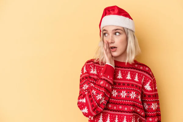 黄色の背景に隔離されたクリスマスを祝う若い白人女性は秘密のホットブレーキニュースと脇を見ている — ストック写真