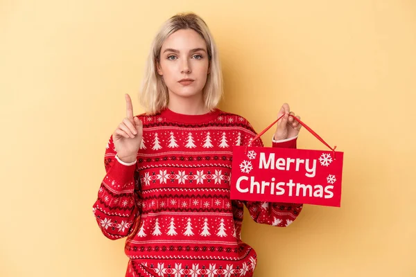 Молодая Белая Женщина Веселым Рождественским Плакатом Желтом Фоне Показывает Номер — стоковое фото