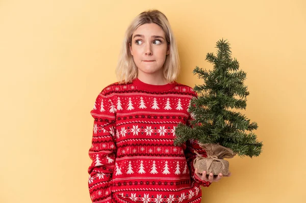 Mladá Běloška Drží Malý Vánoční Stromek Izolovaný Žlutém Pozadí Zmatený — Stock fotografie
