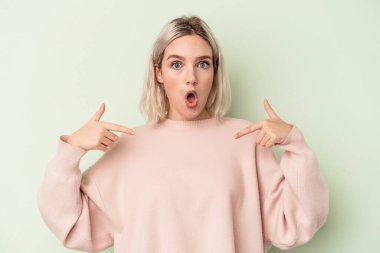 Genç beyaz kadın yeşil arka planda izole edilmiş. Parmakları aşağıda, olumlu hisler içinde..