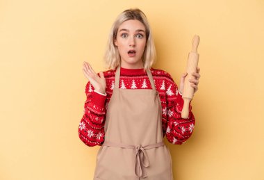Kafkasyalı genç fırıncı kadın Noel için kurabiye yapıyor. Sarı arka planda izole edilmiş. Şaşırmış ve şok olmuş..