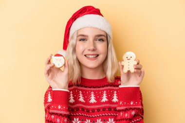 Sarı arka planda izole edilmiş Noel kurabiyeleri tutan beyaz bir kadın.