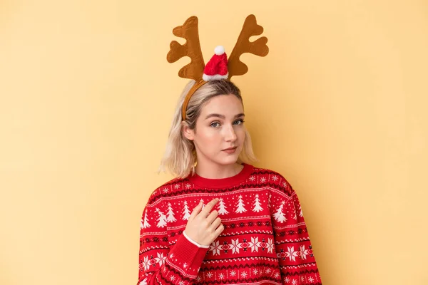 年轻的高加索女人戴着一顶黄色背景的圣诞驯鹿帽 手指着你 好像邀请你走近些 — 图库照片