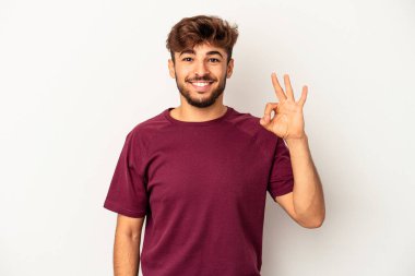 Genç melez adam, gri arka planda izole edilmiş bir şekilde göz açıp kapayıncaya kadar iyi bir el hareketi yapıyor..