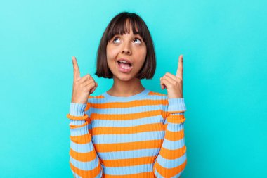Mavi arka planda izole edilmiş genç melez kadın iki parmağı da boş bir alan gösteriyor..