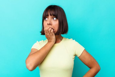 Mavi arka planda izole edilmiş, tırnak yiyen, gergin ve endişeli genç bir ırk kadını..