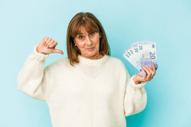 Middle age caucasian woman holding bank notes isolated on blue background feels proud and self confident, example to follow.